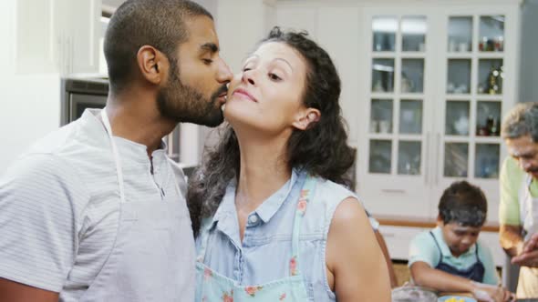 Couple kissing while family preparing cookies in background