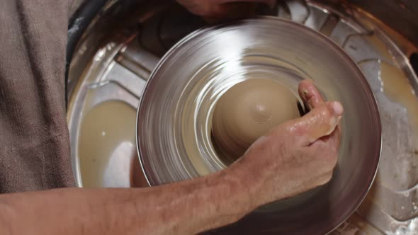 Potter Gives Round Shape to Future Pottery with Two Hands Using Potter's Wheel