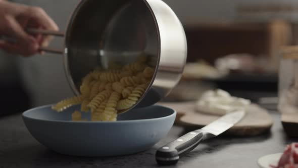 Slow Motion Pour Boiled Fusilli Into Blue Bowl on Concrete Countertop