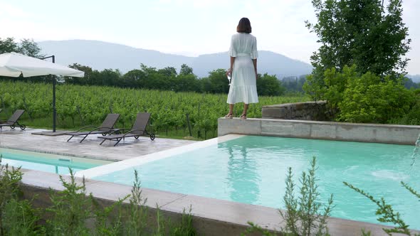 A woman walking with a glass of white wine at a pool traveling at a luxury resort in Italy, Europe