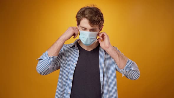 Young Man Takes Off His Medical Face Mask Against Yellow Studio Background