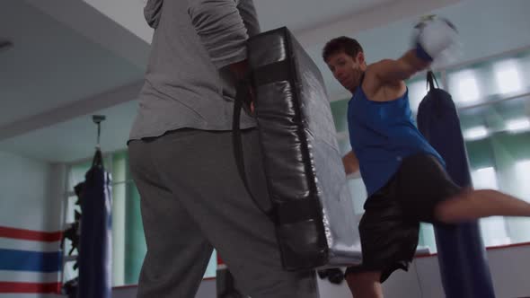 Caucasian man training with coach in boxing gym