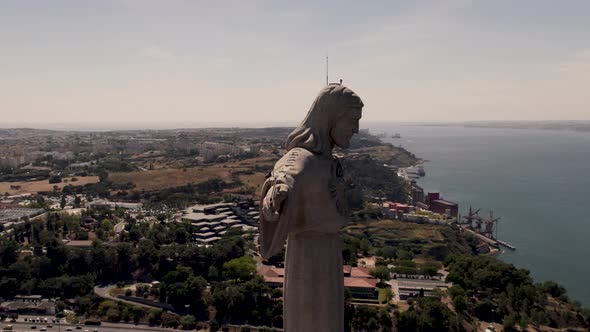 Establishing aerial shot around the statue of Christ the redeemer with open arms facing Lisbon city.