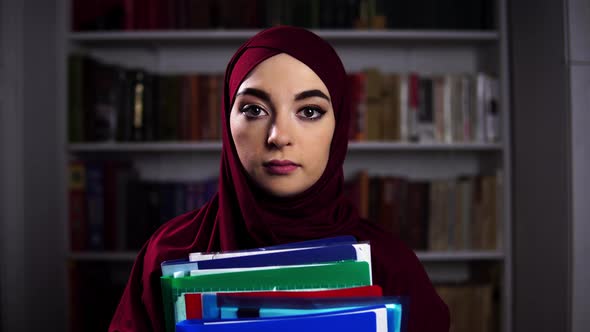 Portrait of a Female Muslim Professor Standing on a Bookshelf Background and Holding Folders