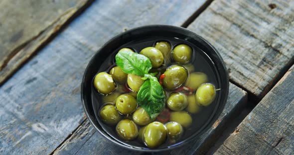 Bowl of green olives in vinegar garnished with herb