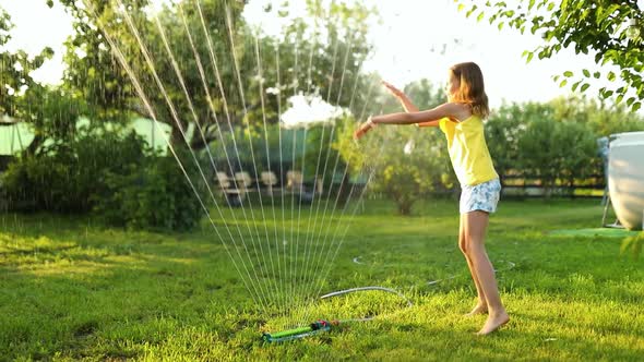 Happy kid girl playing with garden sprinkler run and jump