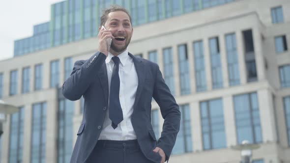 Happy Caucasian Man Hanging Up Phone and Making Victory Gesture. Portrait of Excited Young