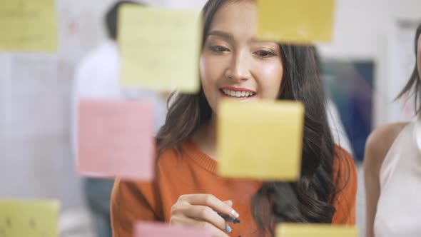 Asian business creative team meeting by use post it notes to share idea on glass wall.