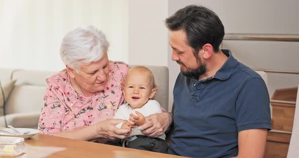 Elderly Woman is Holding Grandson on Lap Her Son is Sitting Next to Her They