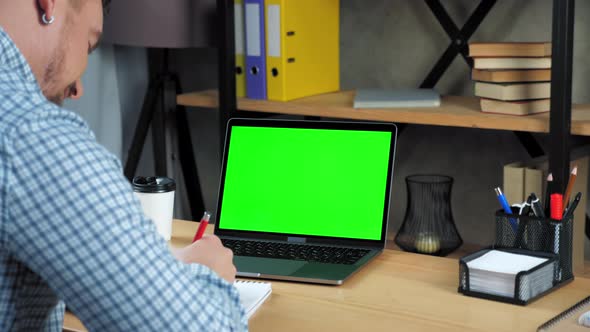 Green screen laptop concept: Smiling businessman writes to-do list in notebook