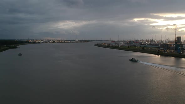 Small boat sailing away near industrial buildings on Antwerp harbor during stormy sunset