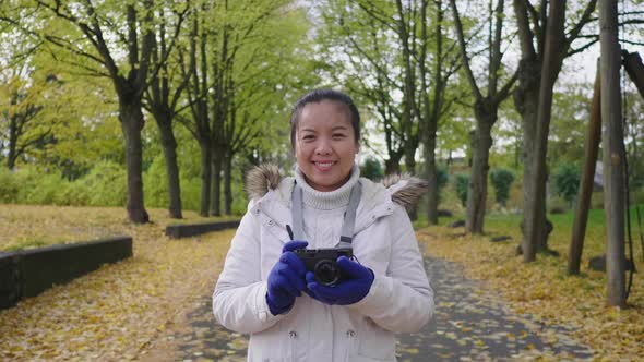 Asian woman holding camera standing in the park in Autumn