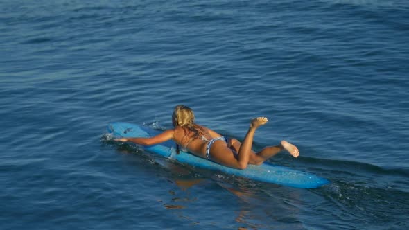 A young woman surfing in a bikini on a longboard surfboard.