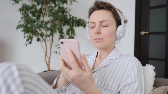 Young Female Relaxing At Home Listening Music On Smartphone And Wearing Headphones