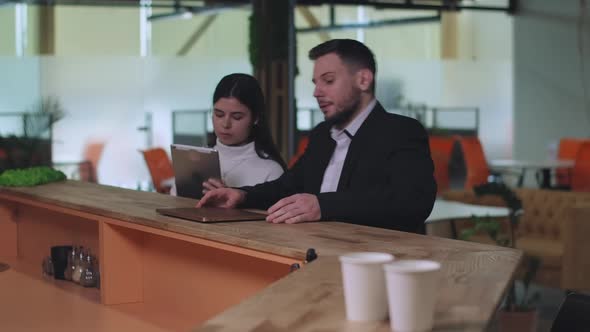 Portrait of Concentrated Young Woman Surfing Internet on Tablet As Focused Man Joining Colleague at