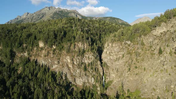 Aerial dolly left flying over Corbata Blanca waterfall hiding between mountains covered in pine tree