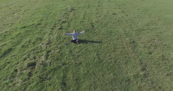 Low Orbital Flight Around Man on Green Grass with Notebook Pad at Yellow Rural Field