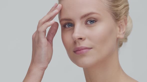 Studio portrait of young, beautiful and natural blond woman applying skin care cream. F