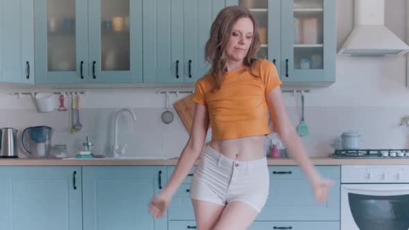 A Beautiful Woman in White Shorts is Relaxing at Home Dancing in the Kitchen