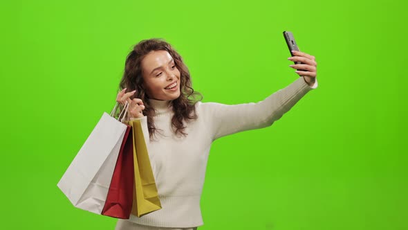 A Woman is Taking a Selfie on a Smartphone and Holding Shopping Bags in Her Hands