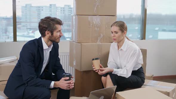 Moving to a New Office Office Workers Sitting on Cardboard Boxes Communicate and Drinking Coffee the