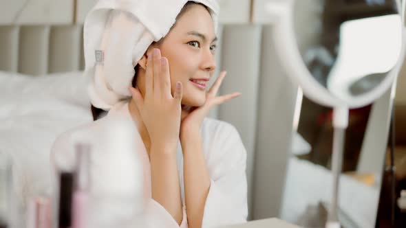 Happy attractive asian woman apply skincare cream on face