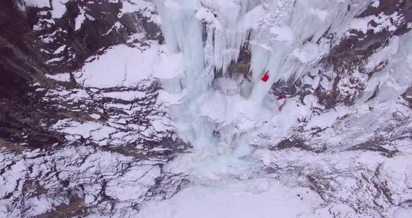 Aerial drone view of a man ice climbing on a frozen waterfall in the mountains