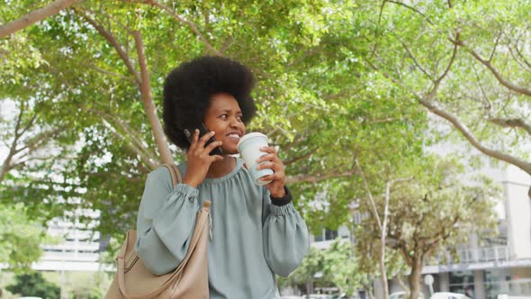 African american businesswoman talking on smartphone and holding takeaway coffee