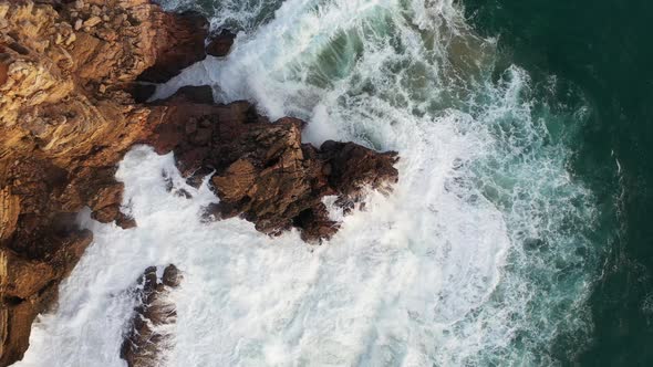 Ocean rock battered by waves in Praia Do Tonel, near Cape Sagres Portugal, Aerial rising circle shot