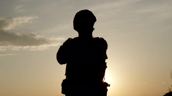 Silhouette of Soldier Against the Sky Stands with His Arms Crossed and Turns Head Towards