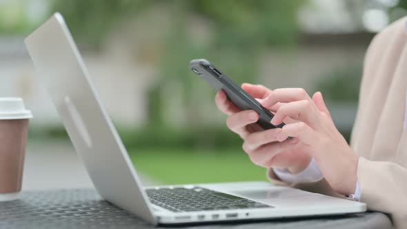 Close Up of Hands of Young Businesswoman with Laptop Using Smartphone