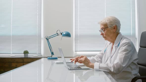 Senior short grey haired lady doctor writes letter on contemporary laptop