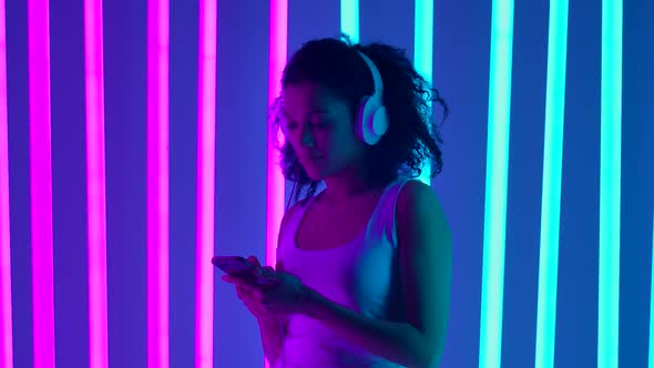 Portrait of a African American Woman in Big White Headphones in a Studio Lit By Neon Tubes