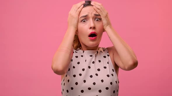 Frightened Woman Grabs Her Head on a Background of a Pink Wall.