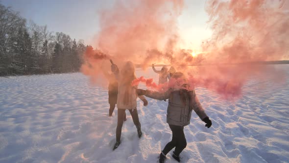 Girls Friends Run Across the Winter Field with Colored Smoke