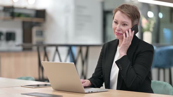Old Businesswoman with Laptop Talking on Smartphone