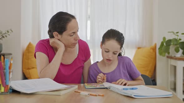 Mother helping her young daughter prepare homework during homeschooling