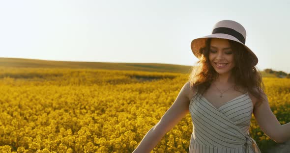 A Smiling Girl Is Walking Across the Field Holding a Hat and Running Her Hand Over the Flowers