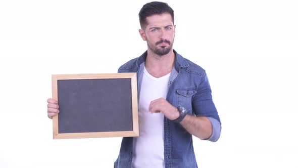 Stressed Young Bearded Hipster Man Holding Blackboard and Giving Thumbs Down