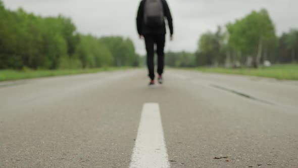 A Male Tourist Walks Along the Center of the Asphalt Road in Windy Rainy Weather