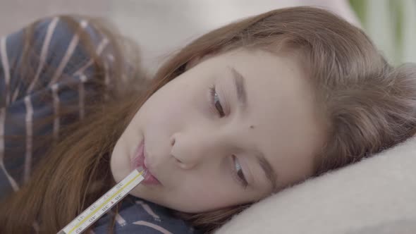 Close Up Sad Sick Girl Lying in Bed with a Thermometer in Mouth. Concept of a Sick Child. Medicine