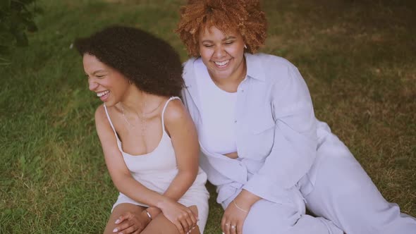 Young Beautiful Happy Lesbian African American Couple Sitting on Green Grass Hugging Outside at