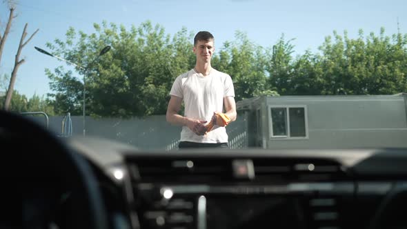 Satisfied Caucasian Young Man Admiring Clean Automobile at Car Wash Service Outdoors