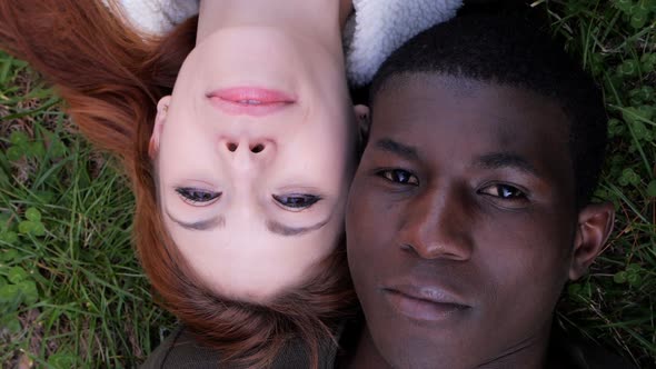 Mixed love concept.Interracial young couple lying on lawn opening eyes closed