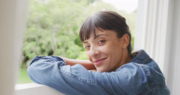 Portrait of happy caucasian woman looking through window and wearing jacket in living room