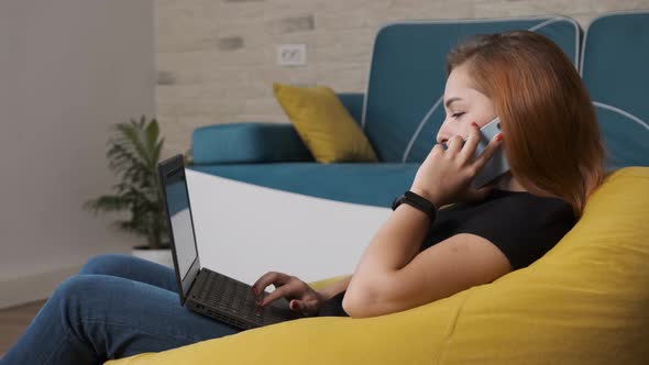 Young Woman Is Working at the Laptop While Is Talking on the Phone