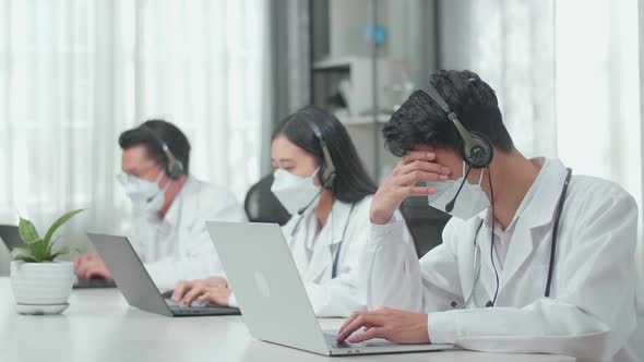 A Man Of Three Asian Doctors In Masks Working As Call Centre Agent And Headache