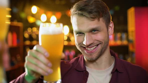 Smiling Man Clinking Beer Glasses With Friend, Enjoying Results Time in Pub