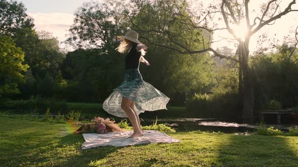 Joyful Woman Dancing & Spinning on Outdoor Picnic Blanket - Sun Flare Glow at Sunset