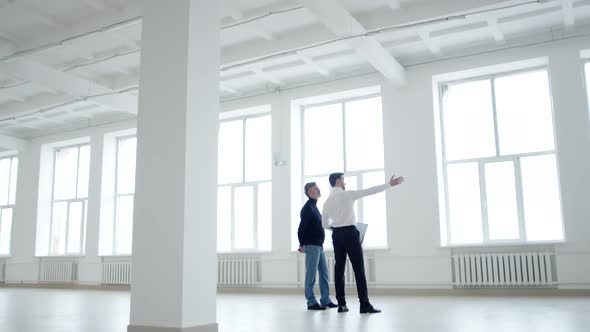 Businessman and Realtor Discuss Contract While Inspecting an Office Space for Rent Side View